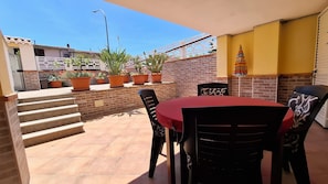 A patio with a table and chairs, potted plants, a brick wall, and a staircase. - Apartment " Sa Casaritza" 850 meters from the beach (La Caletta, Siniscola)