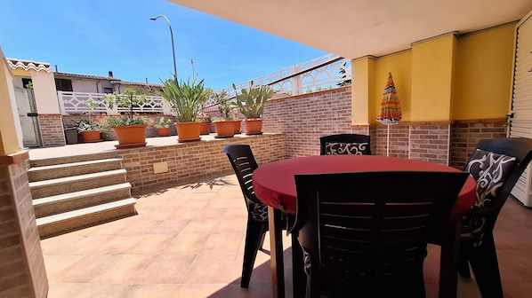 A patio with a table and chairs, potted plants, a brick wall, and a staircase.