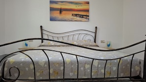 A bed with a metal frame, a patterned bedspread, and a painting of a sunset over water on the wall. - Apartment " Sa Casaritza" 850 meters from the beach (La Caletta, Siniscola)