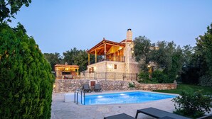 En stenvilla med swimmingpool, udendørs møbler og en overdækket terrasse.