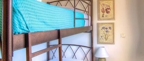 Una cama litera con estructura de madera, una mesita de noche con lámpara, y dos ilustraciones botánicas enmarcadas en la pared.