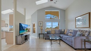 A spacious living room with a large TV, a sofa, and a glass coffee table.