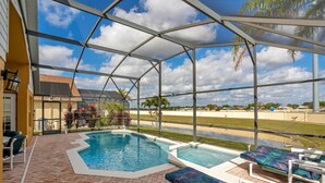A covered pool area with a hot tub, lounge chairs, and a view of the surrounding landscape.