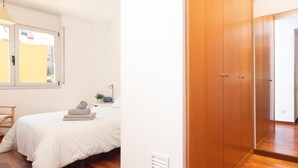 Un dormitorio con cama, ventana, armario de madera y una mesita de noche con lámpara.
