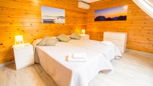 A cozy wooden cabin bedroom with two beds, a nightstand, a dresser, and two wall-mounted pictures.