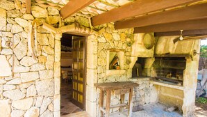 A stone-walled room with a fireplace, a wooden bench, and a door leading to another room.