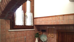 Een keuken met een spoelbak, raam met kantgordijnen, betegelde spatwand en houten keukengerei aan de muur.