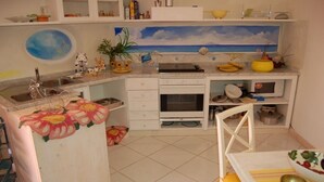 Une cuisine compacte équipée d’un évier, d’une cuisinière et d’un four à micro-ondes, un coin repas avec une table et des chaises, et un tableau décoratif représentant une scène de plage, placé au-dessus du comptoir.