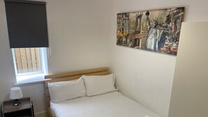 Ein Schlafzimmer mit einem Bett, einem Nachttisch, einer Lampe, einem Gemälde der Freiheitsstatue und einem Fenster mit Jalousien.