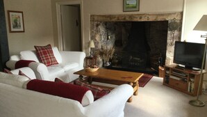A living room with a fireplace, white sofa, red cushions, a wooden coffee table, and a television on a wooden stand.
