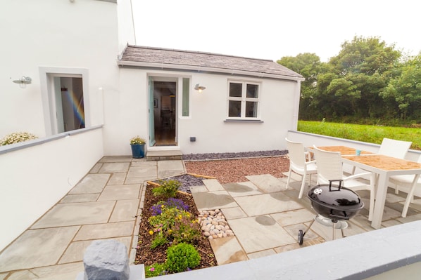 A patio with a barbecue grill, outdoor seating, and a garden bed with flowers.
