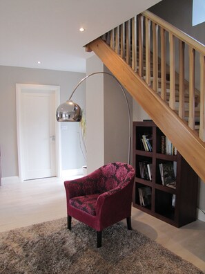 A modern living room with a wooden staircase, a red armchair, a floor lamp, and a bookshelf. - 3 bedroom, sleeps 6, beautiful Village in the centre of Ireland (Multyfarnham)