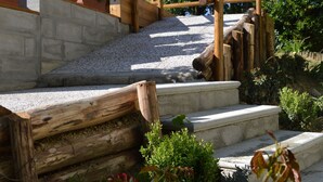 A wooden staircase with a wooden railing, surrounded by greenery and flowers.