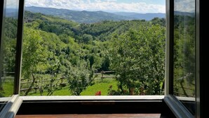A room with a large window offering a view of a lush valley with trees and distant hills.