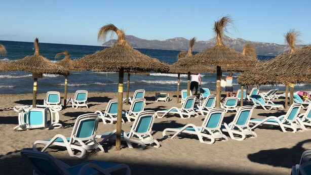 A beach with rows of white lounge chairs and thatched umbrellas, with the ocean and mountains in the background. - Can Biel, cosy  house located 100 metres from the beach (Can Picafort)