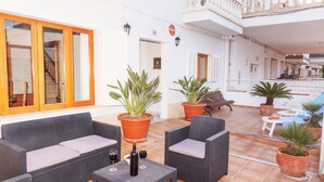 A spacious outdoor area with wicker furniture, potted plants, and a staircase leading to an upper level. - Can Biel, cosy  house located 100 metres from the beach (Can Picafort)