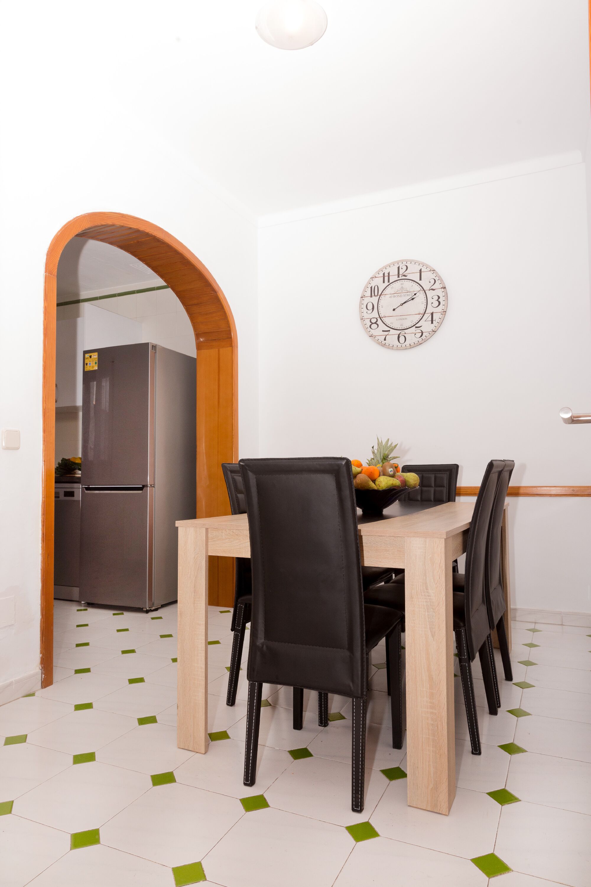 Een eetgedeelte met een houten tafel, zwarte stoelen en een schaal met fruit.