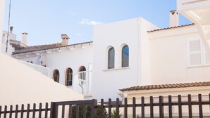 A white building with a tiled roof, a balcony, and a fence in the foreground. - Can Biel, cosy  house located 100 metres from the beach (Can Picafort)