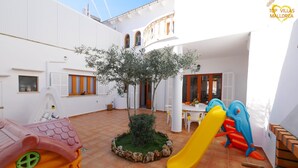 A courtyard with a small tree, a yellow slide, and a play area. - Can Biel, cosy  house located 100 metres from the beach (Can Picafort)