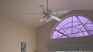 A living room with a TV, speakers, a ceiling fan, a large window, and a view of a swimming pool. - Lakeview Villa in Kissimmee, pool & hot tub, free pool heat, close to Disney (Kissimmee)