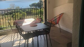 Uma varanda com mesa e cadeiras, um ventilador de teto e vista para o mar.