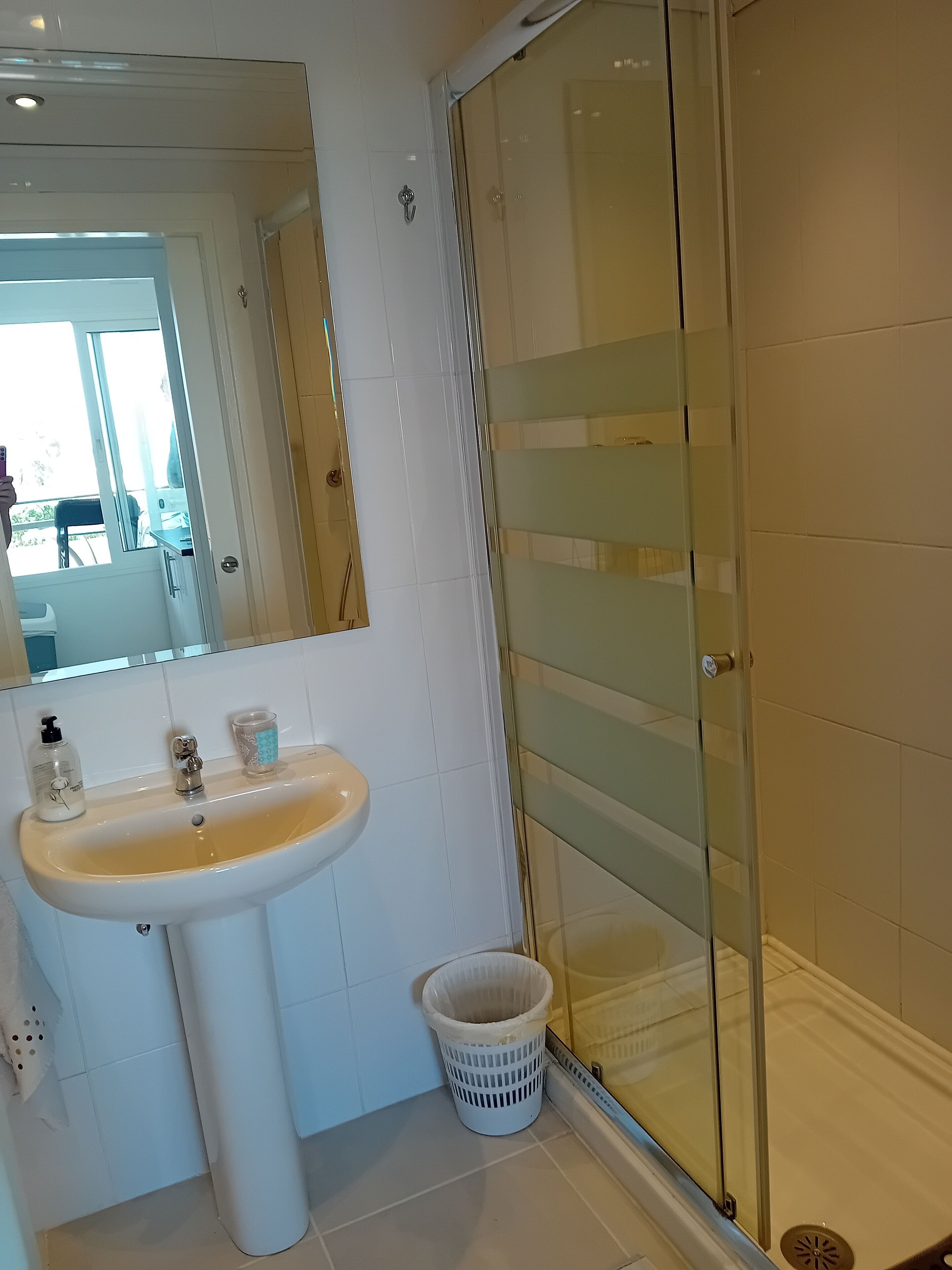 Une salle de bain avec un lavabo blanc, une cabine de douche en verre et une poubelle blanche.