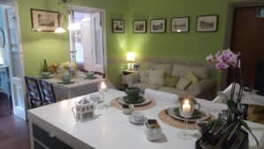 Uma área de refeições com uma mesa posta para dois, com uma vela, um bule e um vaso com flores.