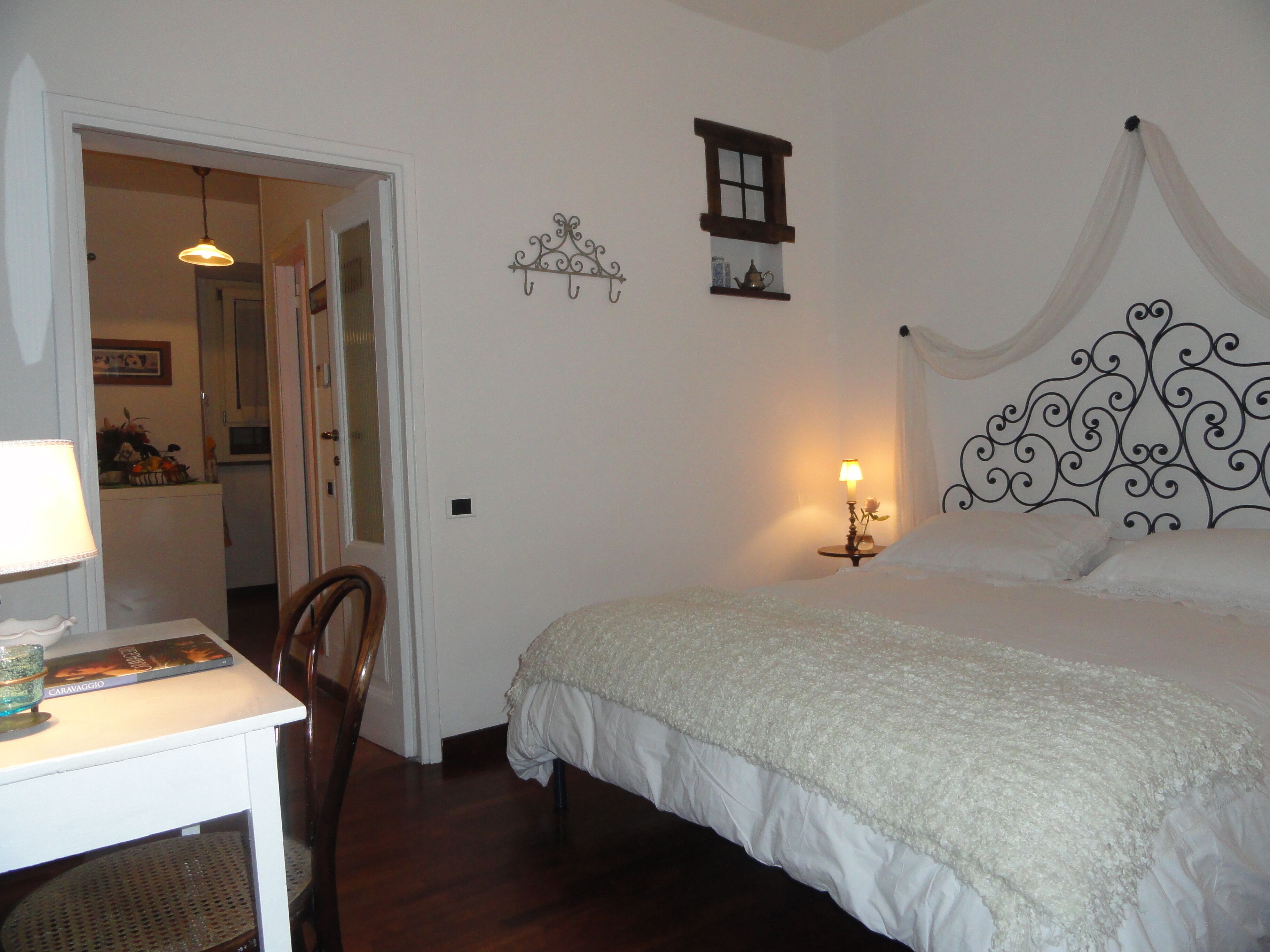 A bedroom with a bed, a desk with a lamp, a chair, a small window, and a decorative wall piece.