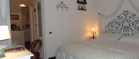 A bedroom with a bed, a desk with a lamp, a chair, a small window, and a decorative wall piece.
