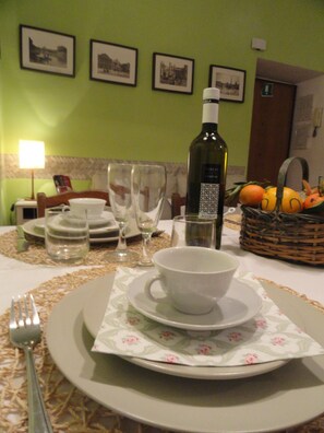A dining table set with plates, bowls, and glasses, a bottle of wine, and a basket of fruit.