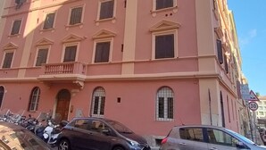 Um edifício de vários andares com fachada rosa, várias janelas com persianas e um estacionamento com carros.