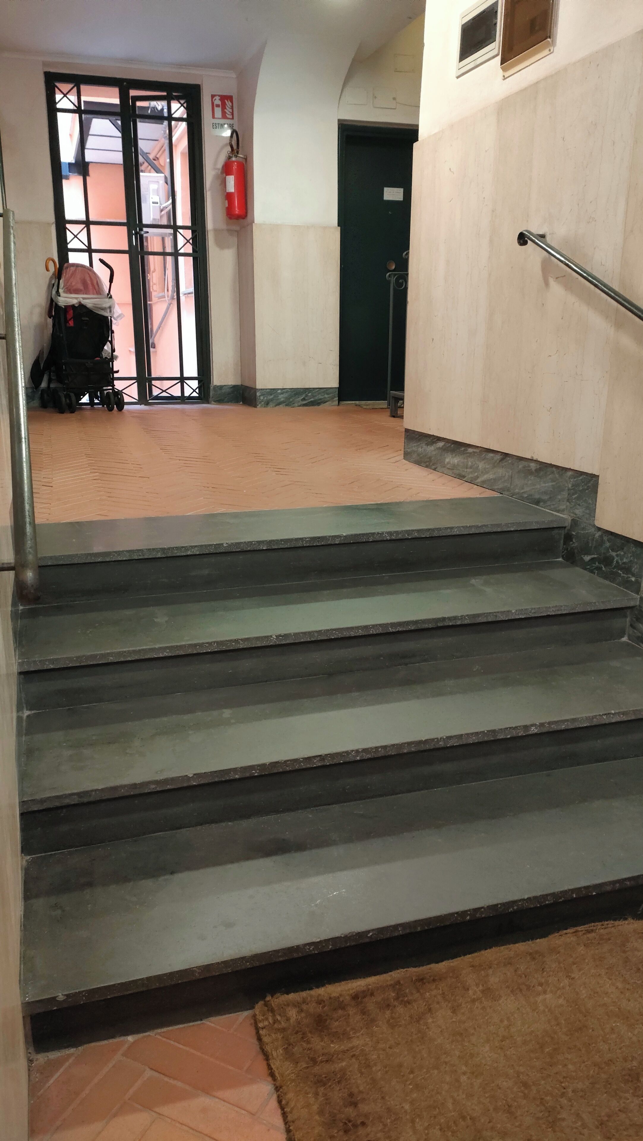 A set of dark grey stairs leading to an upper floor, with a fire extinguisher mounted on the wall to the left.