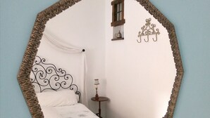 Quarto com cama, mesa de cabeceira, espelho e um adorno na parede.