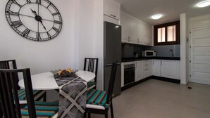A modern kitchen with white cabinets, a large wall clock, and a dining area with a round table and chairs.