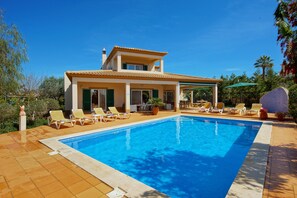 Una casa de dos pisos con piscina, zona de estar exterior y un patio cubierto.