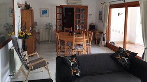 A cozy living room with a sofa, a dining table with chairs, a wooden cabinet, and a radiator. - "Casa Montana" Holiday house for 6 persons with Private Pool (Puerto Pollensa)