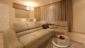 Ein modernes Wohnzimmer mit einem beigefarbenen Ecksofa, einem Glastisch und einer Deckenleuchte.