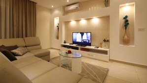 Ein modernes Wohnzimmer mit einem beigefarbenen Sofa, einem Glastisch, einem Flachbildfernseher und dekorativen Vasen.