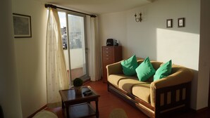 Un soggiorno con divano, tavolino, mobile e una porta scorrevole in vetro che dà su un balcone.