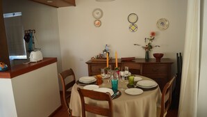 Zona pranzo con tavolo rotondo apparecchiato per quattro, circondato da sedie di legno. Si vedono piatti, bicchieri e un vaso con fiori sul tavolo.