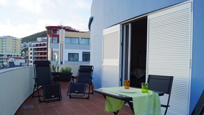 Un balcone con due poltrone, un tavolo con tovaglia verde e una finestra con persiana bianca.