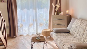 Un salon comprenant un canapé, une table basse, un pouf en osier, un meuble en bois et une fenêtre avec des rideaux.