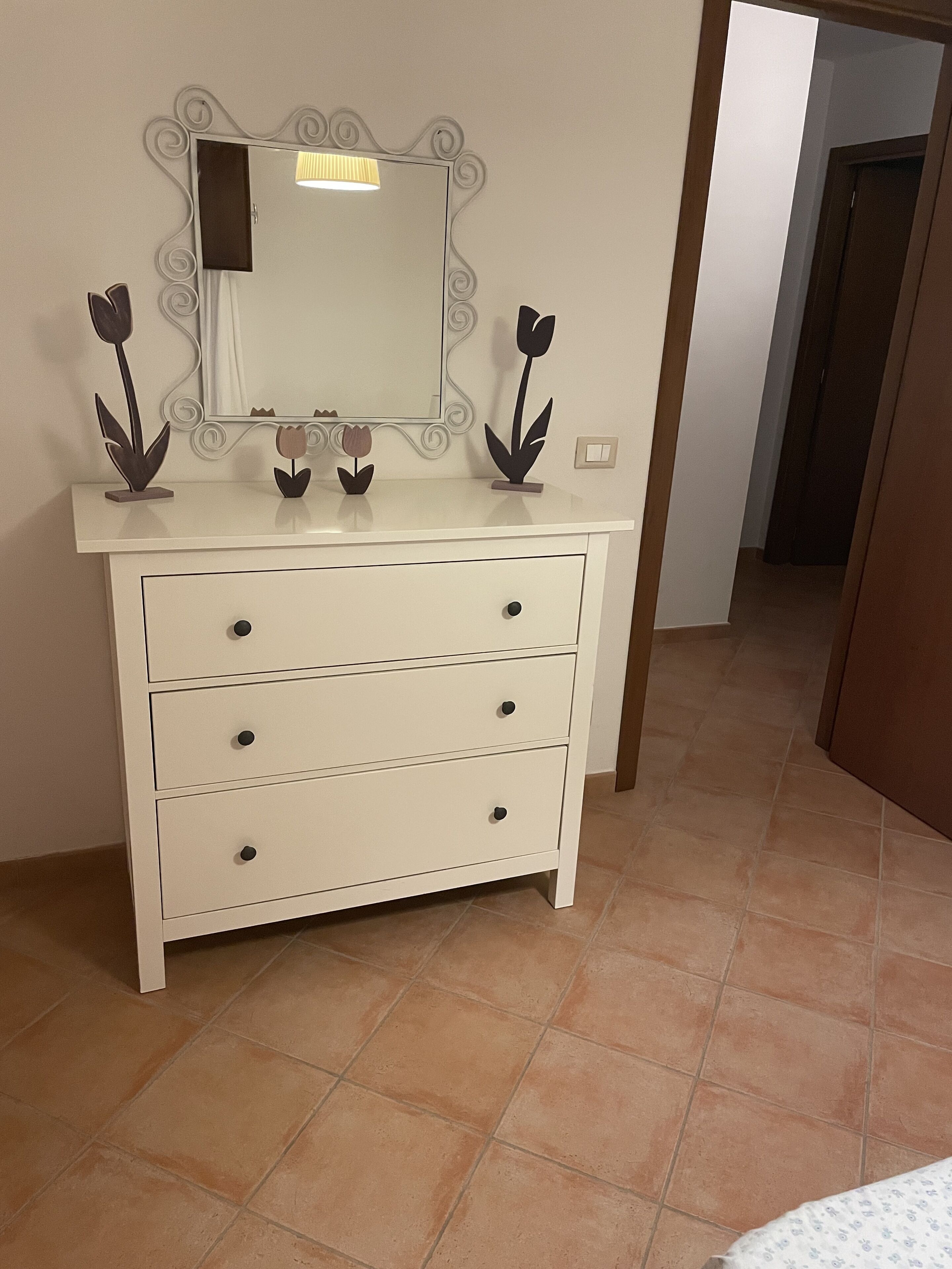 A white dresser with three drawers and a mirror with a decorative frame.