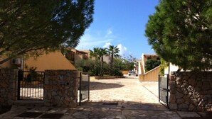 Un camino pavimentado que lleva a una entrada con puerta y muros de piedra, junto a un edificio amarillo.