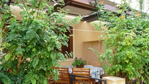 Un patio con una mesa y sillas, rodeado de abundante follaje y una pérgola de madera.