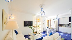 A modern living room with a sofa, a coffee table, and a TV. There is a dining area with a table and chairs. The kitchen is visible with white cabinets and blue tiles. - Il canto delle sirene,  in the heart of Amalfi Coast, parking Property overview (Conca dei Marini)