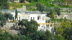 A white building with a stone facade, surrounded by lush greenery and trees. - Il canto delle sirene,  in the heart of Amalfi Coast, parking Property overview (Conca dei Marini)