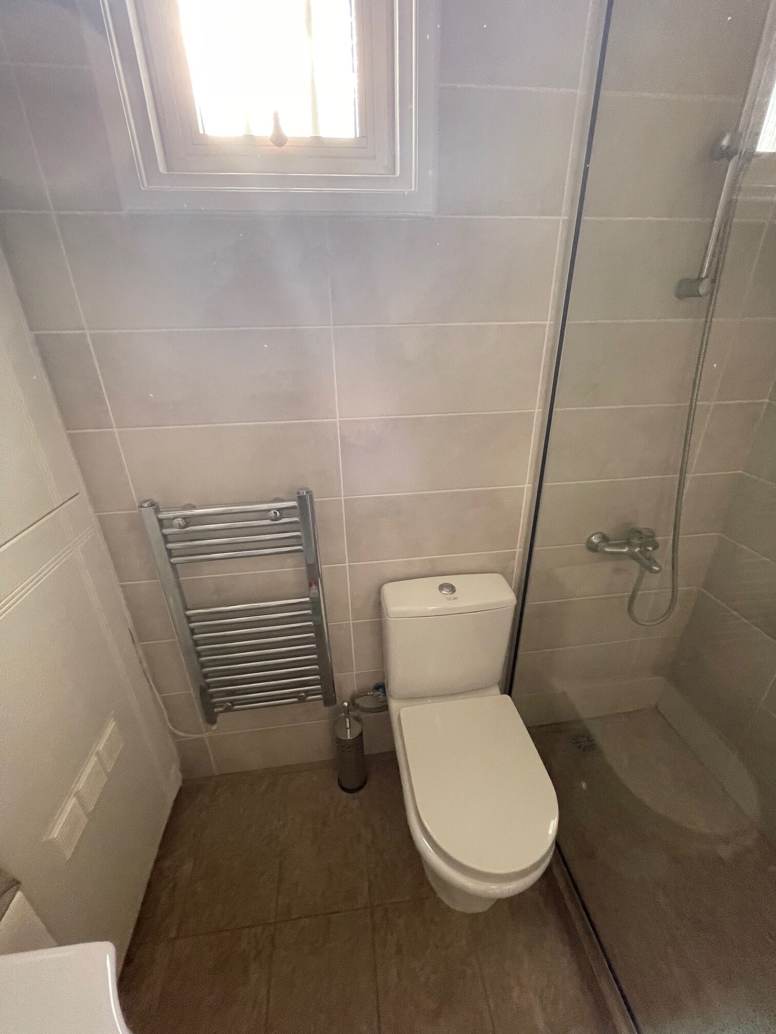 A small, tiled bathroom with a toilet, a shower, and a towel rack.