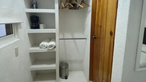 A small, narrow hallway with a wooden door, white walls, and a built-in closet with shelves, a hanging rack, and a trash can.