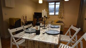 A dining area with a rustic wooden table set for four, including wine glasses and a bottle of wine. - Recently renovated 2 bedroom annexe with open plan living room and kitchen. (Stoney Middleton)
